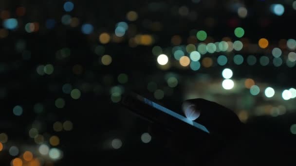 Женщина с мобильным телефоном против ночного размытого городского пейзажа — стоковое видео