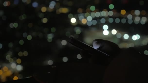 Browsing on smart phone at night, city lights in background — Stock Video