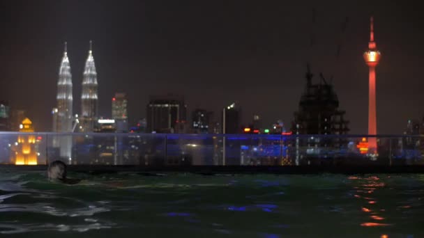 Woman relaxing in rooftop swimming pool at night, Kuala Lumpur — Stockvideo