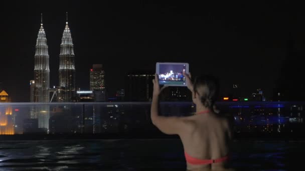 Woman with pad shooting night Kuala Lumpur from rooftop pool — ストック動画