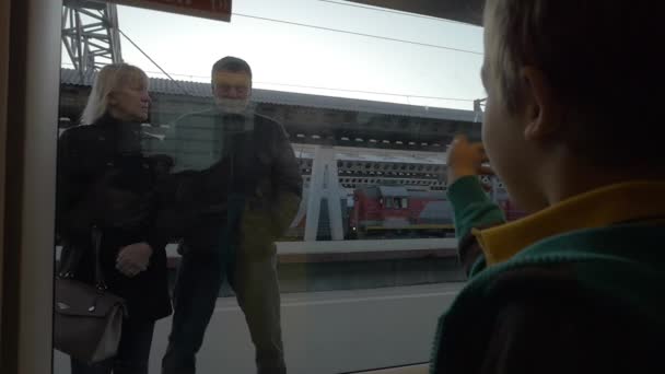 Медленное движение в Санкт-Петербурге, Россия мальчик из окна поезда ждет бабушек и дедушек, которые стоят на платформе — стоковое видео