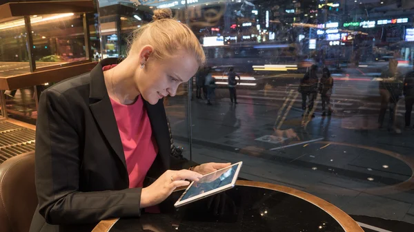 Vrouw met behulp van pad in café door raam met uitzicht op de stad — Stockfoto