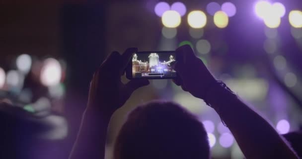 観客の男は屋外音楽コンサートでスマート フォン経由でスポット ライトとステージのパノラマ写真を作る — ストック動画