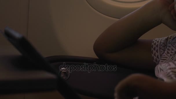 Nahaufnahme eines kleinen Jungen, der im Flugzeug mit einem Touchpad auf dem Tisch spielt — Stockvideo