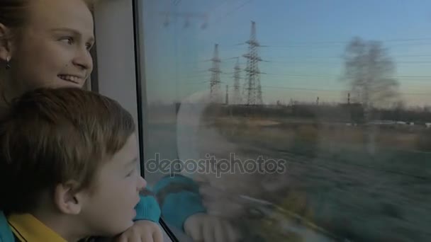 Small boy with mother sitting against window in their rail train place and watching outside — Stock Video