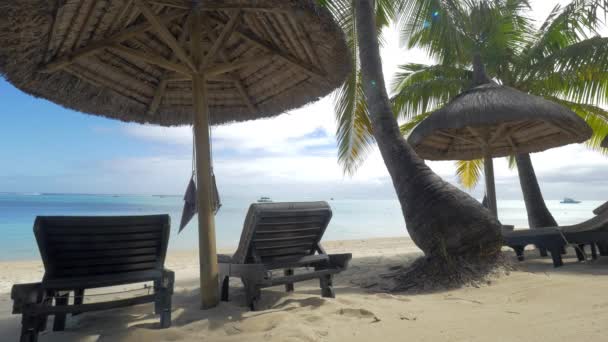 Blick auf leere Chaiselongue in der Nähe einheimischer Sonnenschirme und Palmen gegen blaues Wasser, Mauritius Island — Stockvideo