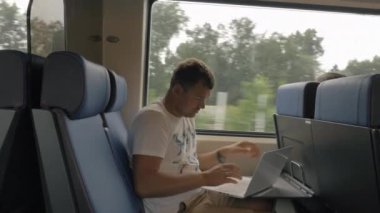 Tren yolculuğunda dizüstü bilgisayar kullanan bir adam.