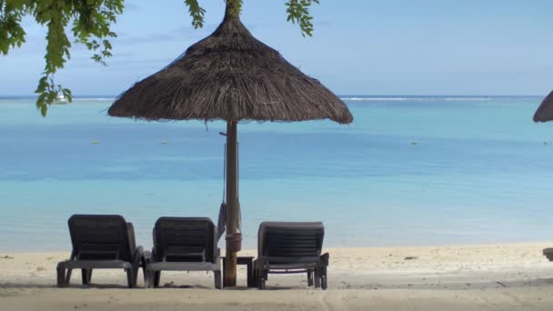 Άποψη της κενής σεζλόνγκ κοντά στην ομπρέλα ιθαγενή ήλιο ενάντια στα γαλάζια νερά, Νήσος Μαυρίκιος — Αρχείο Βίντεο