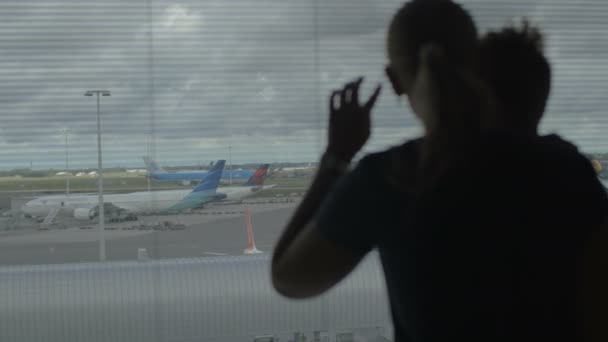 Mother and son looking through airport window — Stock Video