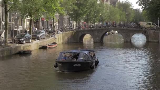 Вид с моста на движение по каналу лодки с людьми, Амстердам, Нидерланды — стоковое видео