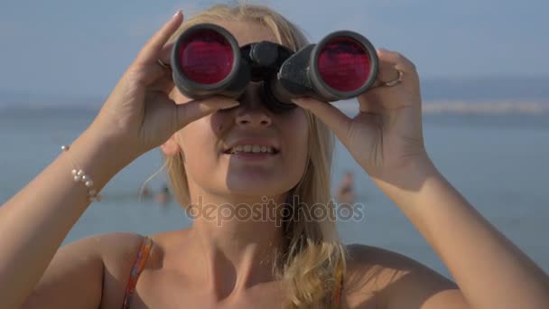 Vista de la mujer rubia mirando con prismáticos contra el mar borroso — Vídeo de stock