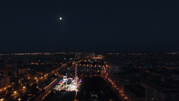 Aerial night view of lighted ferris wheel in amusement park against sky with moon, Valencia, Spain — Stock Video
