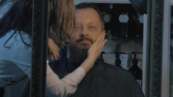 Vista de perto do barbeiro feminino cuidando da barba exuberante do homem. Barbeiro aplicando cosméticos — Vídeo de Stock