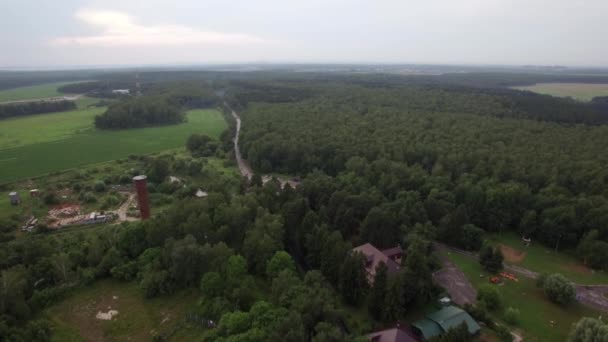 Vol aérien au-dessus de Lukino, Moscou, paysage pittoresque de forêts verdoyantes et de champs, bâtiments ruraux et circulation — Video