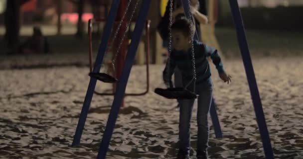 Bambino che si diverte con altalene vuote nel parco giochi la sera — Video Stock