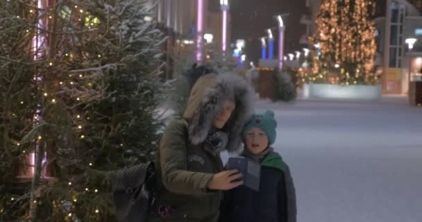 Mamá y el niño haciendo selfie de invierno en la calle con iluminación de Navidad — Vídeos de Stock