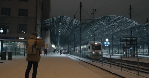 Hombre tomando vídeo móvil de la estación de salida de tren en la noche, Helsinki — Vídeo de stock