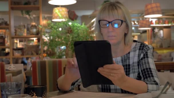 Старша жінка, що серфінг Інтернет на майданчику в кафе — стокове відео