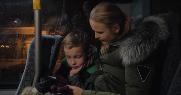 Ребенок с матерью, использующий мобильный телефон в автобусе — стоковое видео