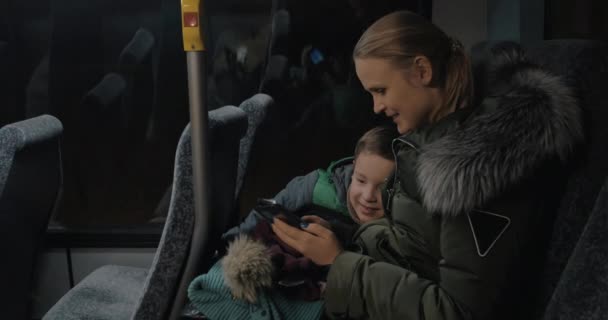 Ребенок и мать путешествуют на автобусе и смотрят на фотографии в сотовом телефоне — стоковое видео