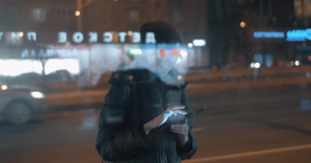 Jovem surfando internet no pad quando espera por ônibus na cidade da noite — Vídeo de Stock