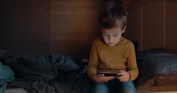 Ребенок с сотовым телефоном сидит на кровати дома — стоковое видео