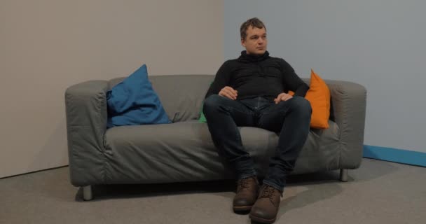 Мужчина сидит на диване в холле и ждет — стоковое видео