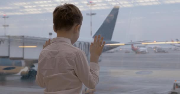 Niño esperando vuelo y mirando aviones a través de la ventana — Vídeos de Stock