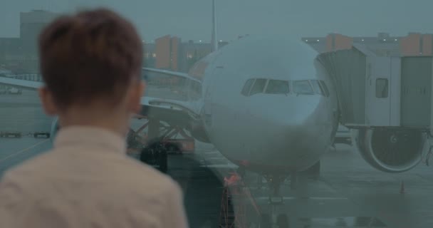 Kid waiting at airport and looking at plane through the window — Stock Video