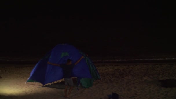 Jóvenes levantando la carpa en la orilla del mar por la noche — Vídeos de Stock