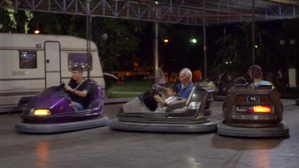 Adultos con niños que se divierten conduciendo coches de parachoques en feria de diversión — Vídeos de Stock