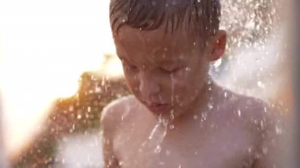 Мальчик принимает пляжный душ на закате — стоковое видео