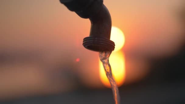 Agua corriendo desde el grifo sobre el fondo de la puesta del sol — Vídeo de stock