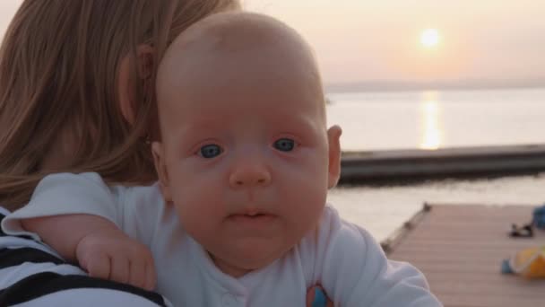 Дитяча дівчинка в руках матері, відкритий на заході сонця — стокове відео
