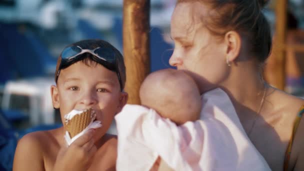 Mère avec bébé et fils aîné à la plage. Garçon manger de la glace — Video
