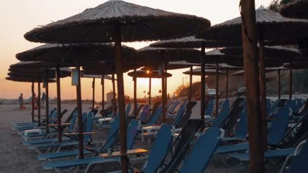 Beach, szalma napernyők és nyugágyak a naplemente, Görögország — Stock videók