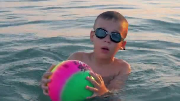 Kind zwemmen in de zee en plezier maken met bal — Stockvideo