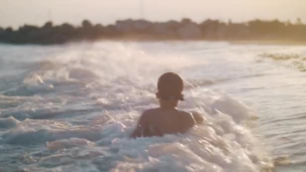Kind badet bei Sonnenuntergang im Meer in Küstennähe — Stockvideo