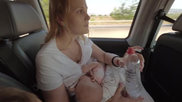 Mum nursing baby and drinking water in moving car — Stock Video