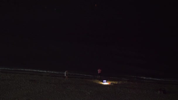 Ночной вид людей, отдыхающих на пляже и глядящих на темное море — стоковое видео
