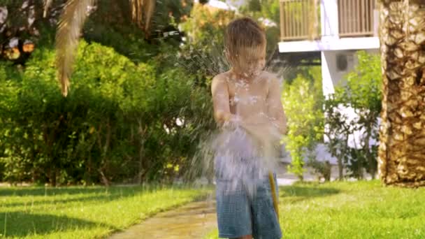 Мальчик поливает газон и промокает. — стоковое видео