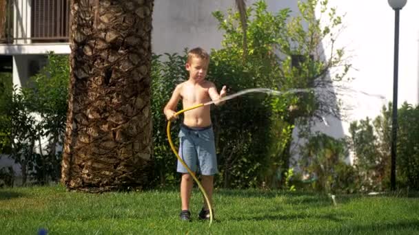 Chico tratando de hacer frente a chorro de agua al regar el césped — Vídeos de Stock