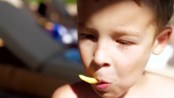 Chico comiendo bocadillos con papas fritas en la playa — Vídeos de Stock