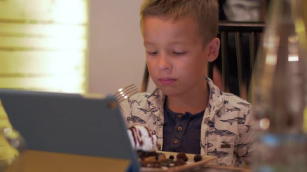 Niño comiendo y mirando almohadilla táctil en la cafetería — Vídeos de Stock