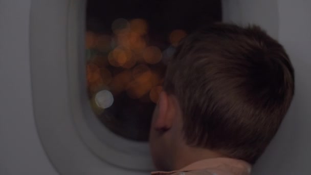 Хлопчик подорожує літаком вночі і дивиться ілюмінатор — стокове відео