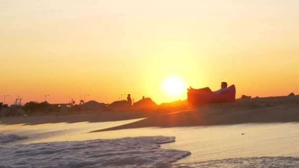 Zonsondergang scène van man ontspannen in opblaasbare zonnebank aan zee — Stockvideo