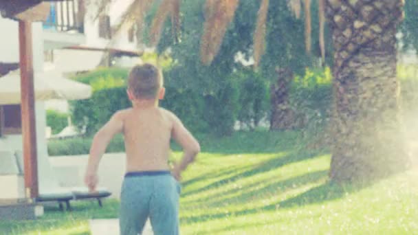 Criança correndo do aspersor no jardim da casa — Vídeo de Stock