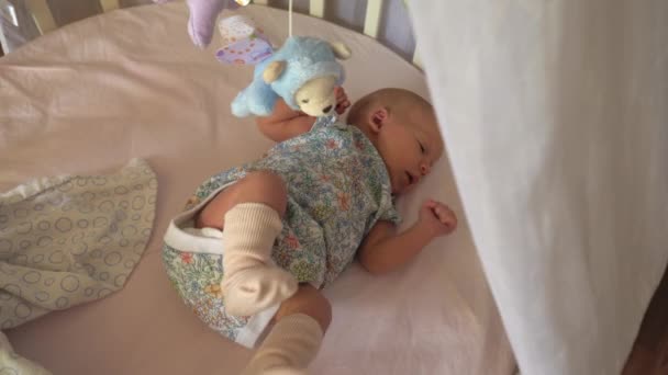 Baby mit Schluckauf liegt in Kinderbett mit Spielmobil — Stockvideo