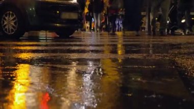 Yağmurlu gece şehirde, insanlar yol geçtikten
