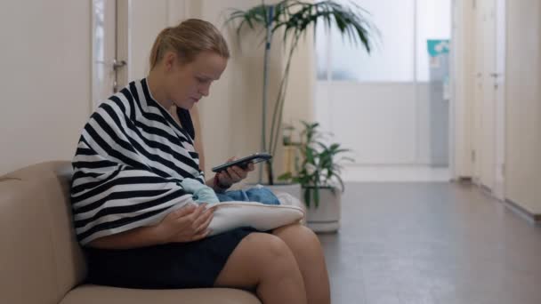 Woman using mobile and nursing baby in child health center — Stock Video